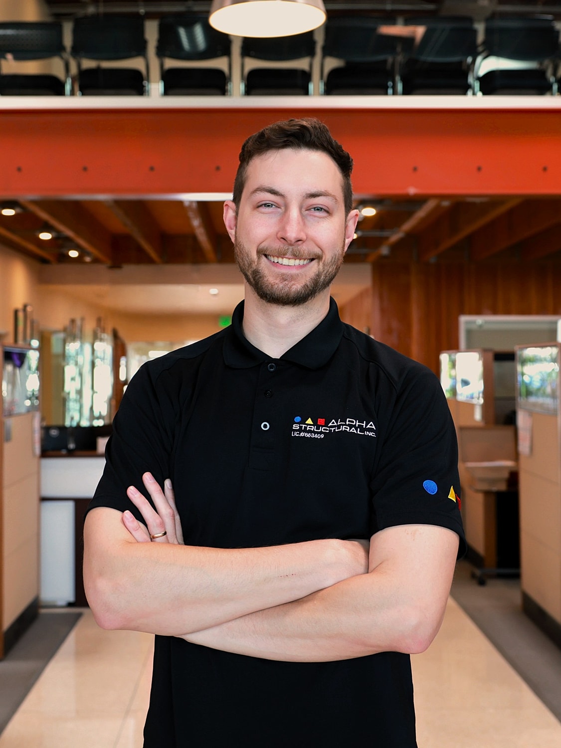 Smiling man in black polo shirt, arms crossed.