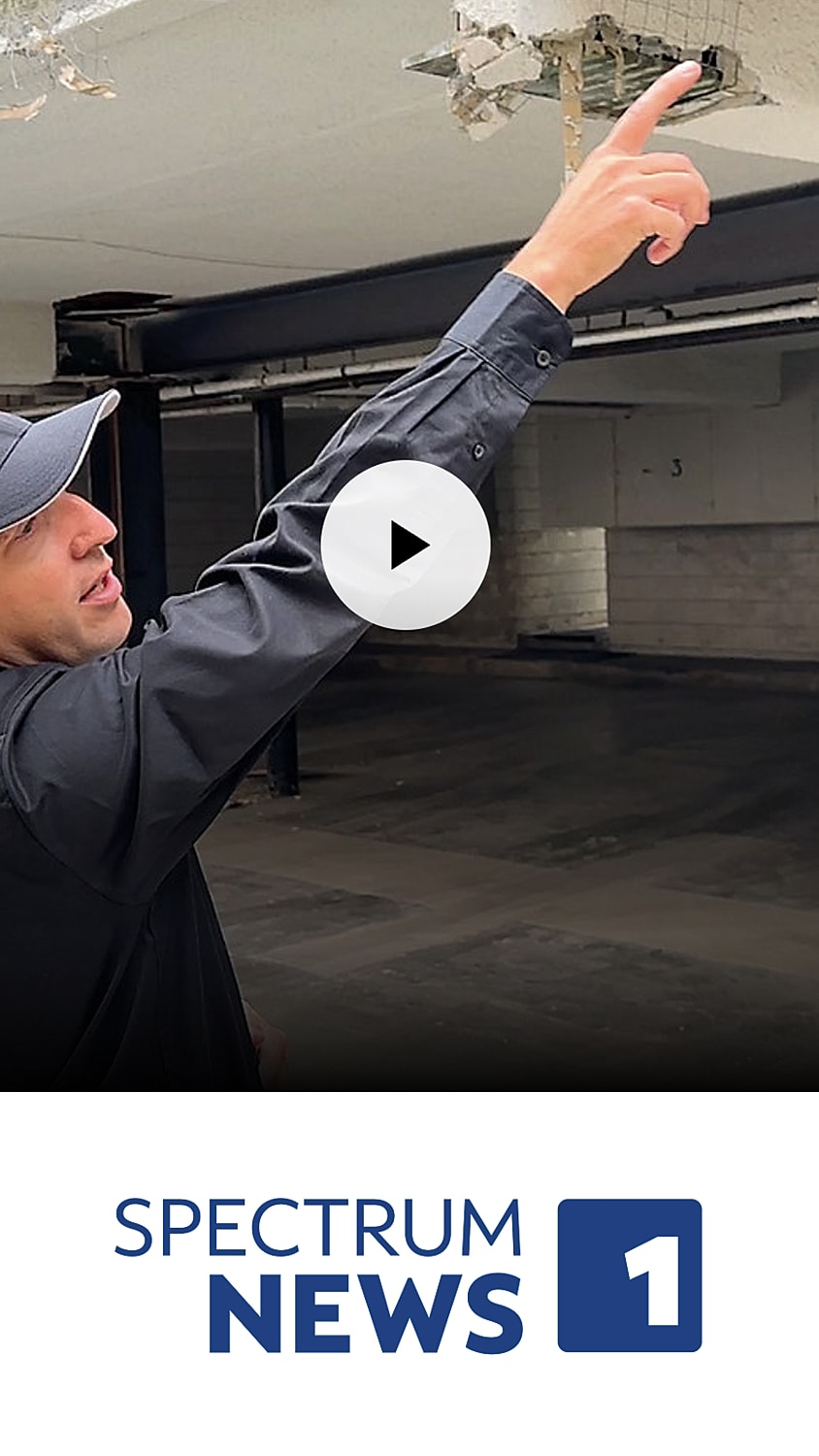 Person pointing at ceiling damage, video play button.