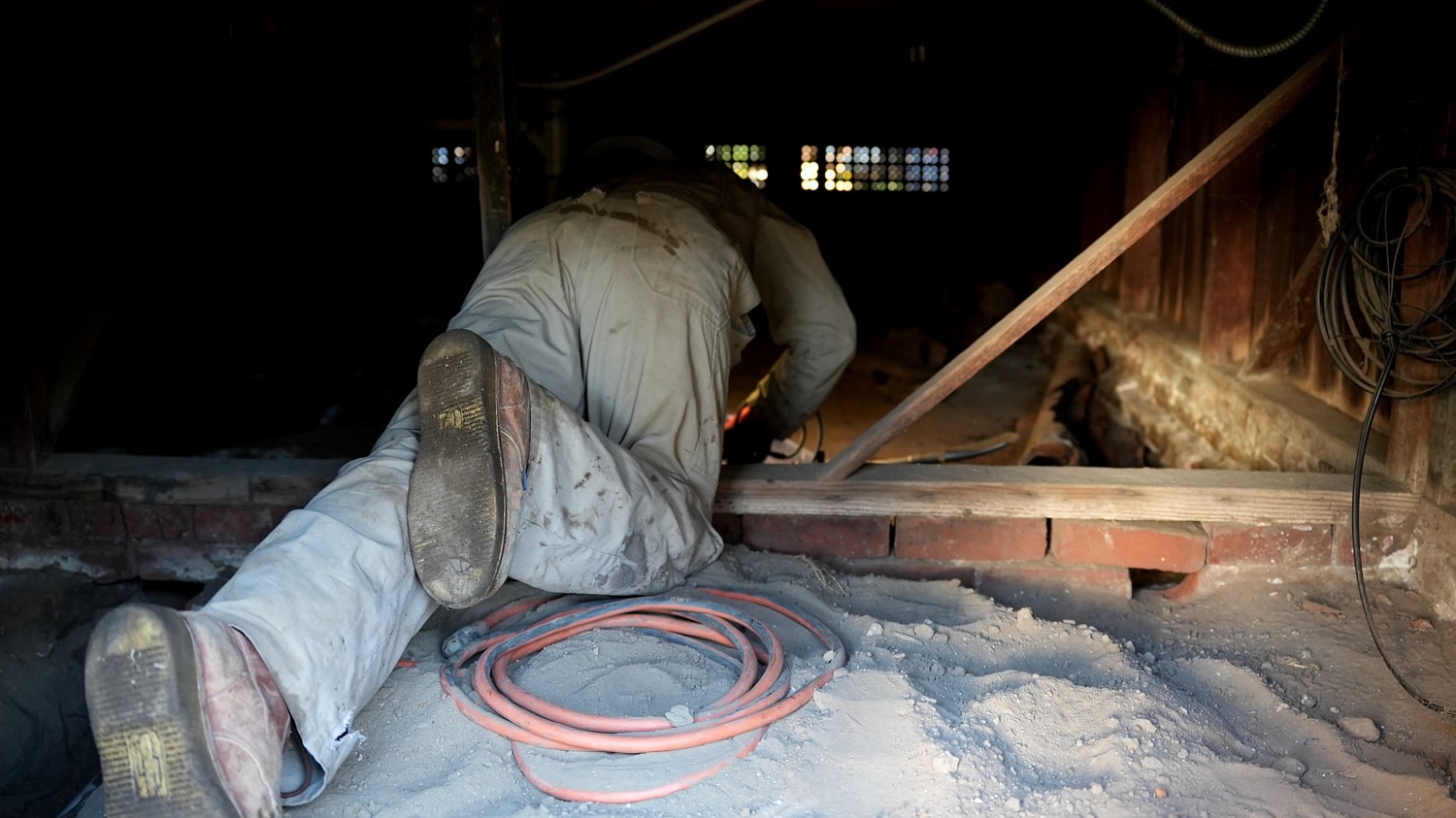 Worker crawling under a structure with tools.