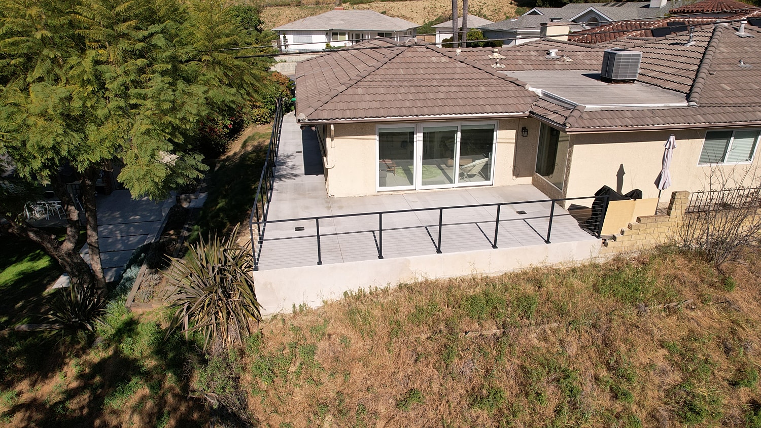 House with patio and railing overlooking greenery.