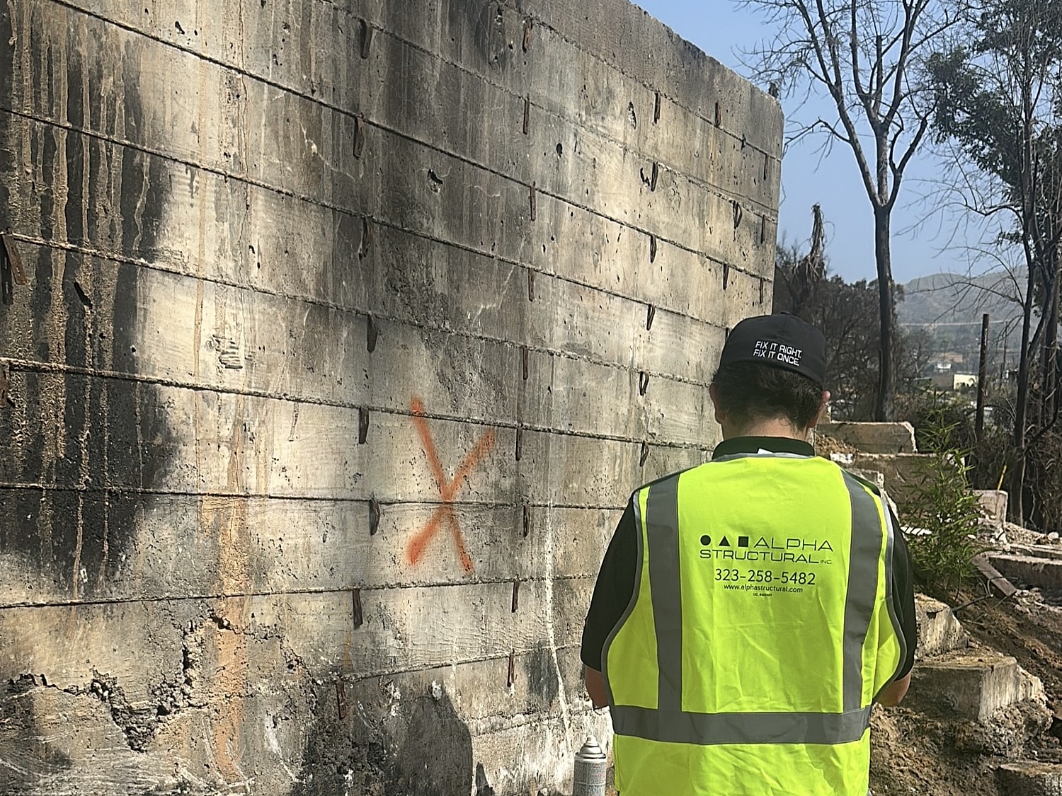 Worker assessing damaged concrete wall structure.