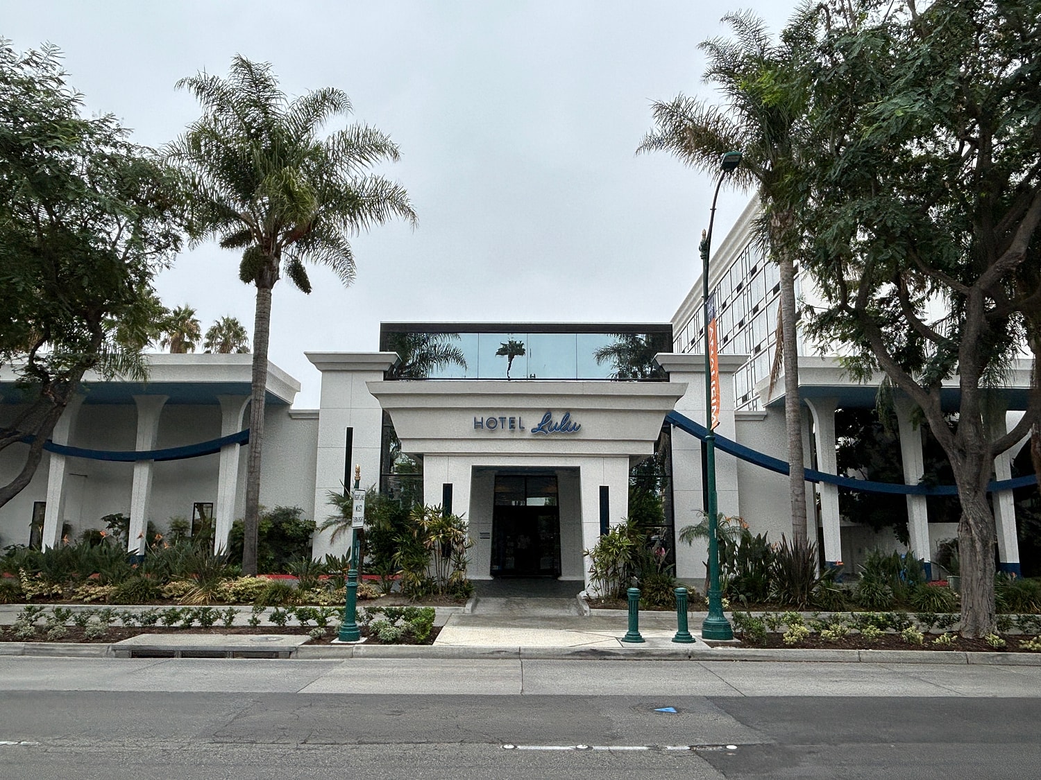Hotel entrance with palm trees and landscaping.