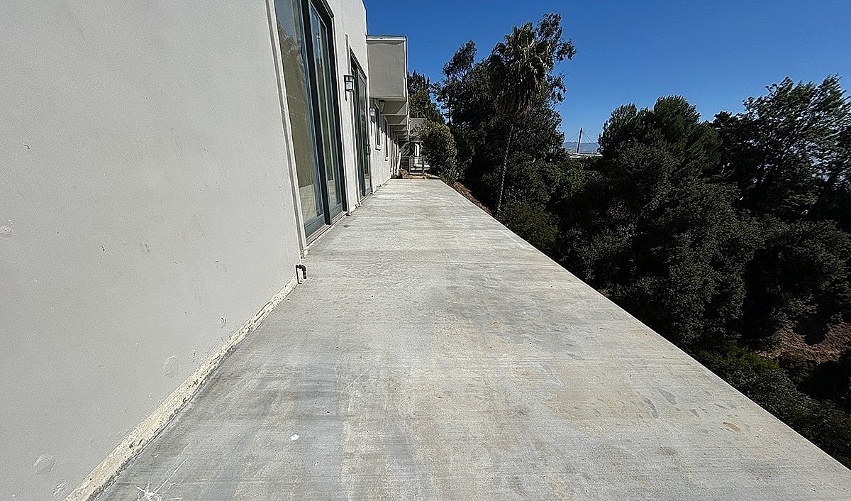 Concrete walkway beside a building, surrounded by trees.