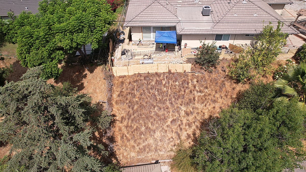 Dry backyard with construction materials and trees.