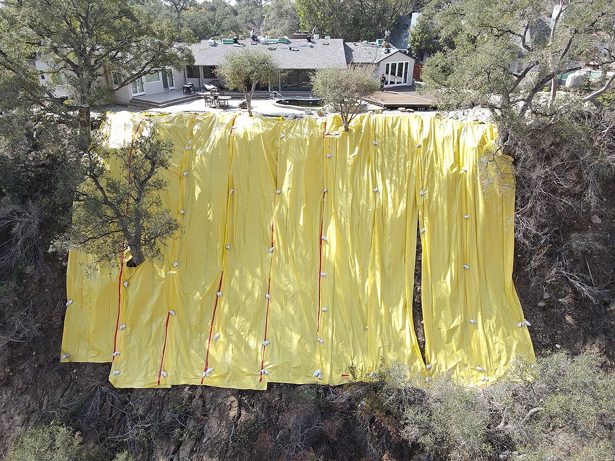 Yellow tarp covering a hillside near a house.