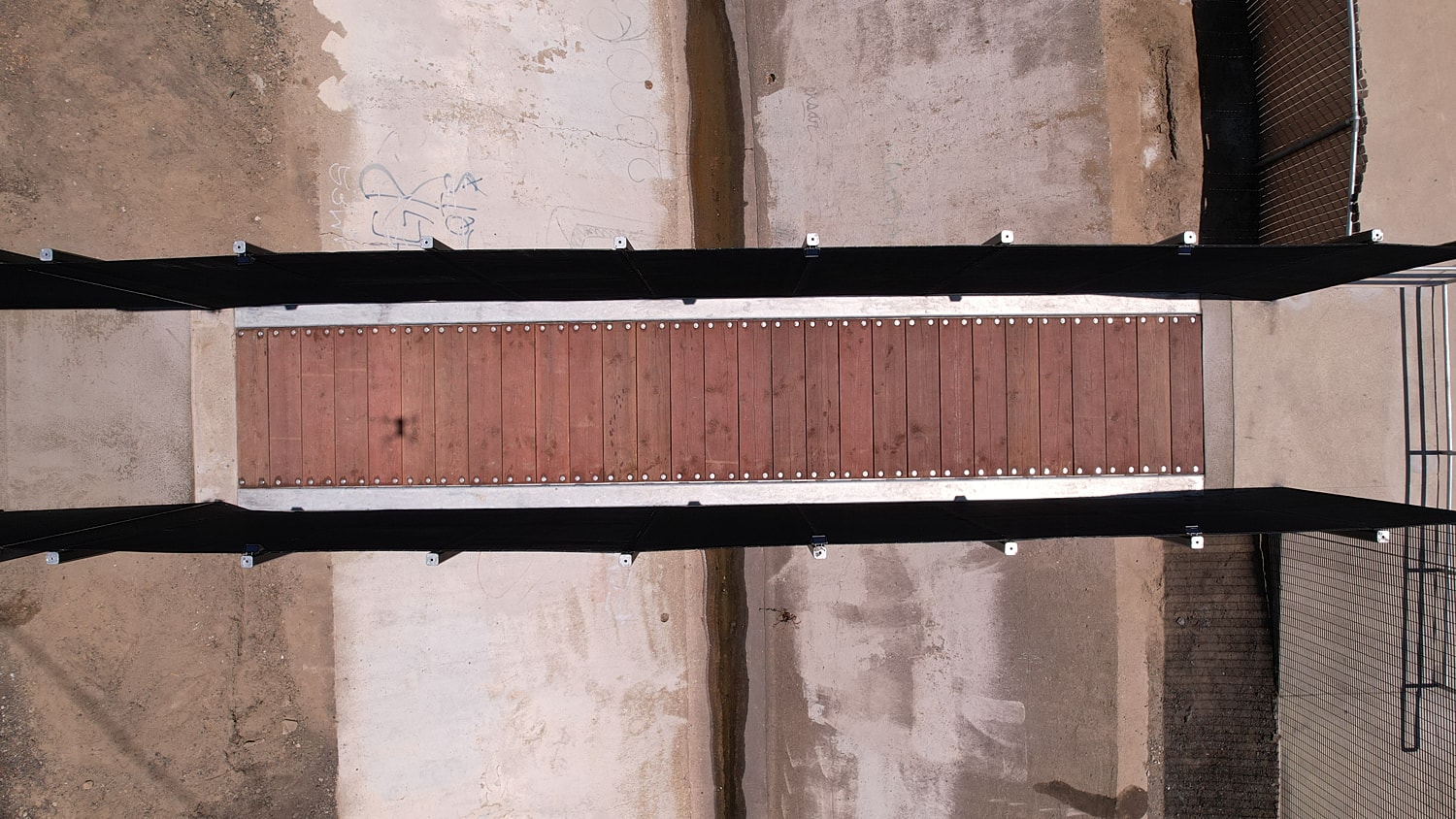Aerial view of wooden bridge over concrete path.