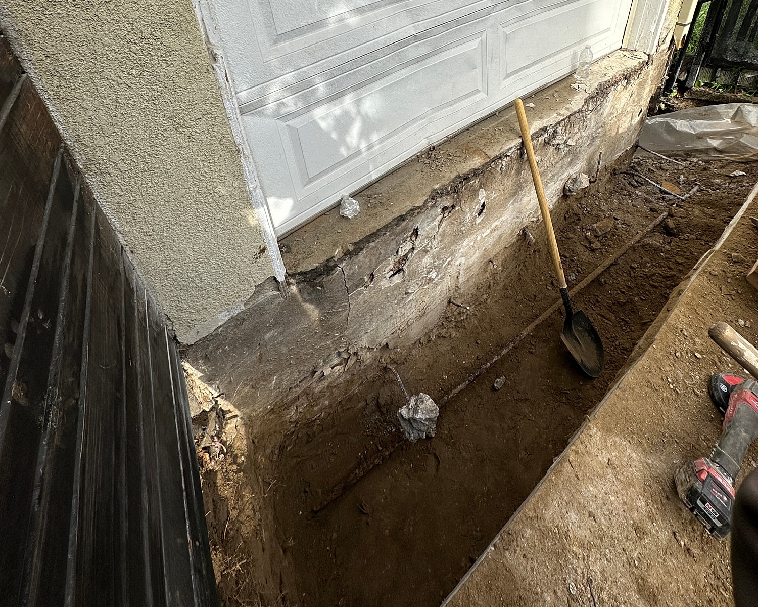 Excavation near a garage foundation with tools.